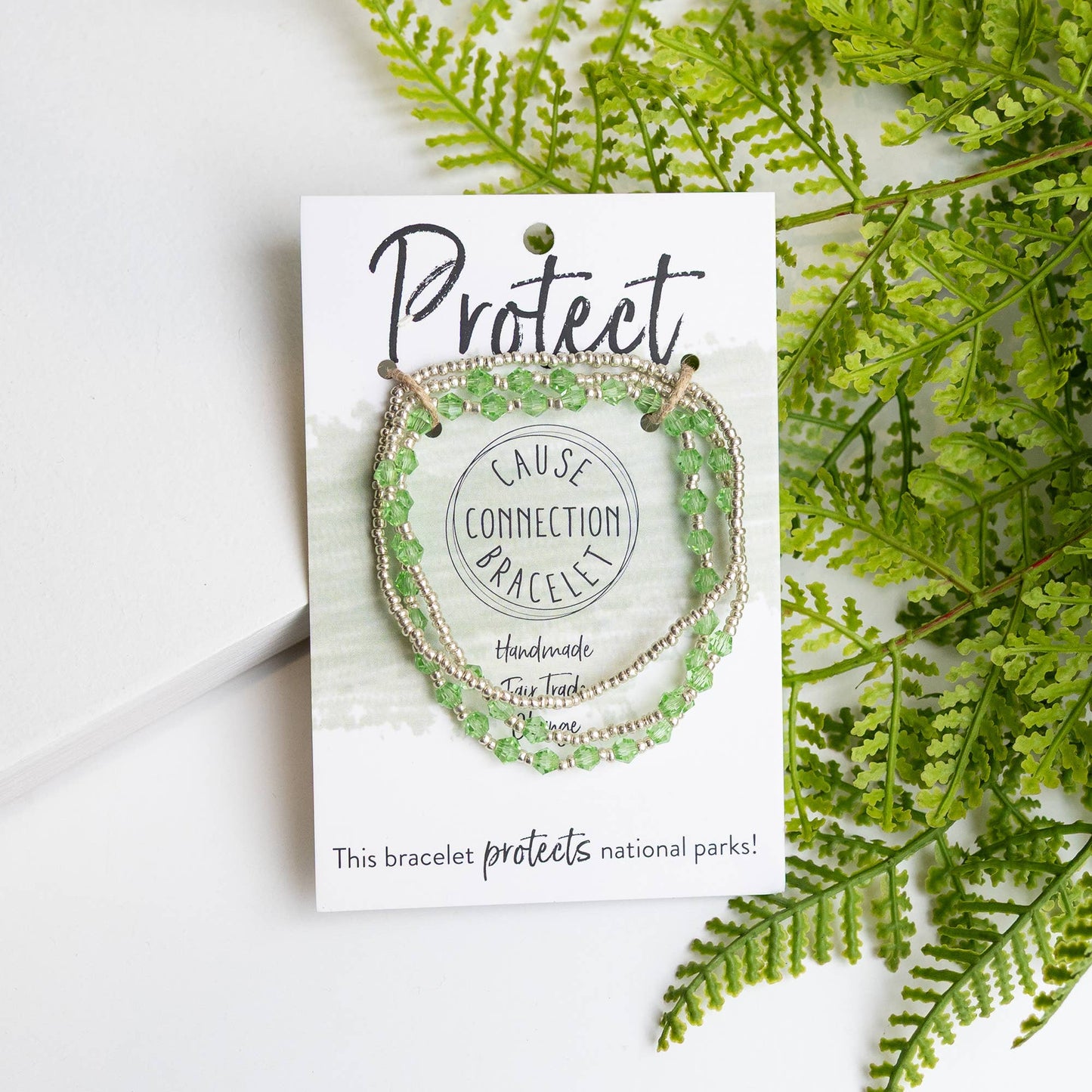 Cause Protect bracelet packaging with green handmade bracelet that protects the rainforest, displayed on a white card with green leaves