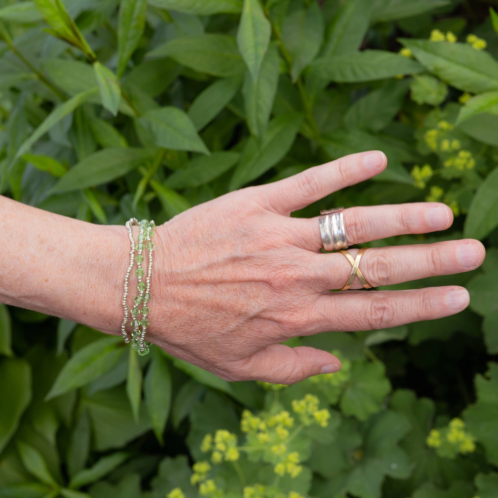 Hand wearing Cause bracelet in green with a green leafy background