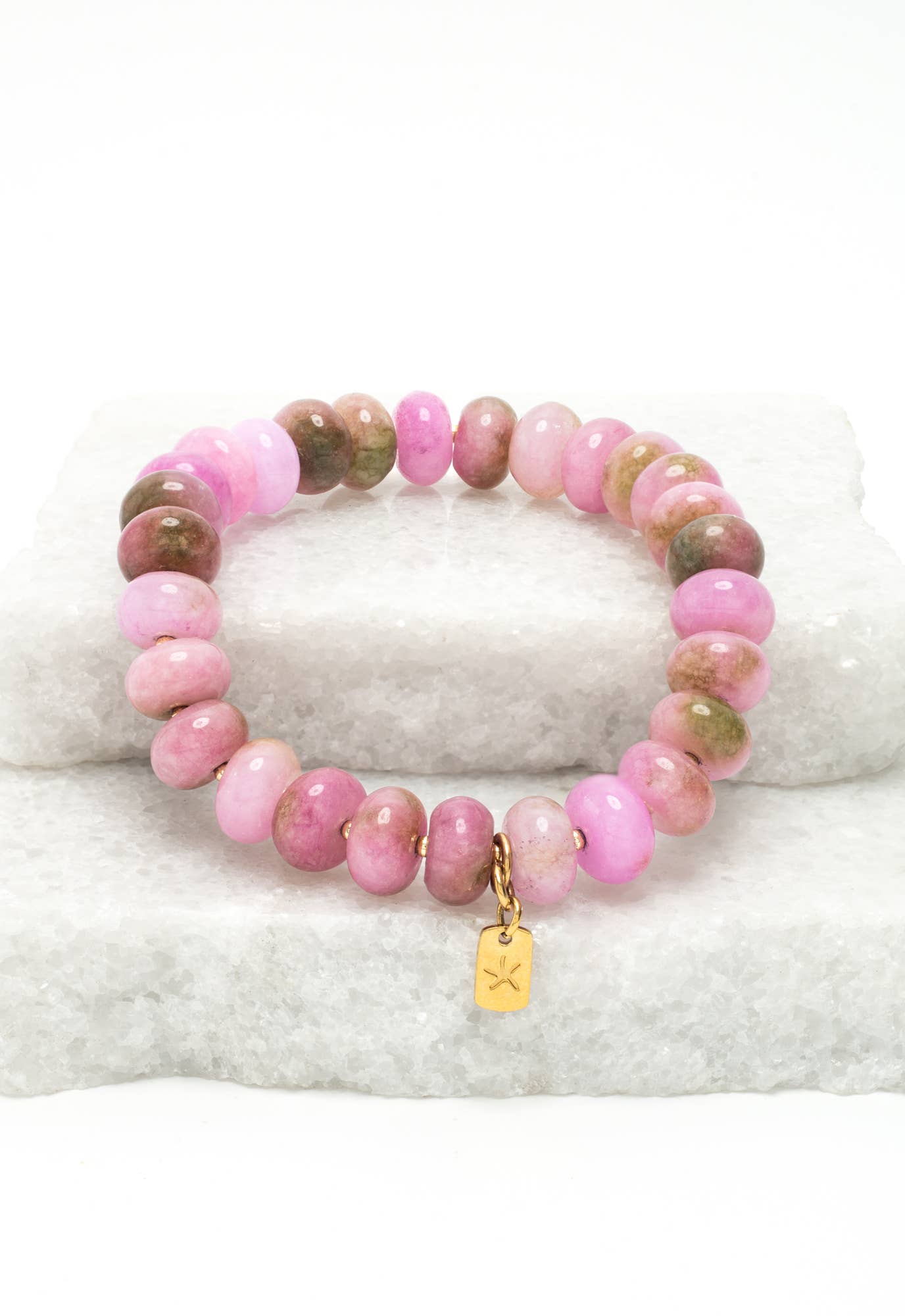 Pink beaded bracelet with a gold tag on a white stone surface