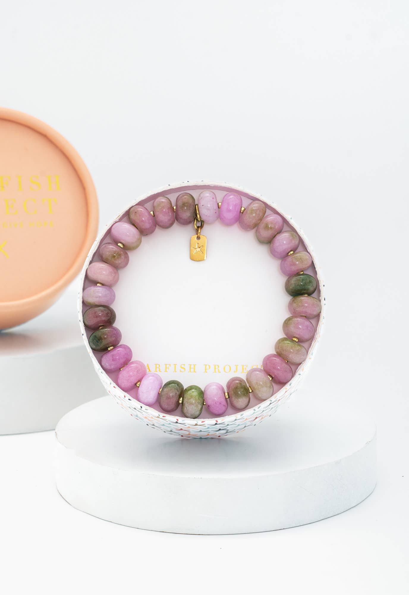 Beaded bracelet with pink and green stones on a white stand, with a pink box in the background.