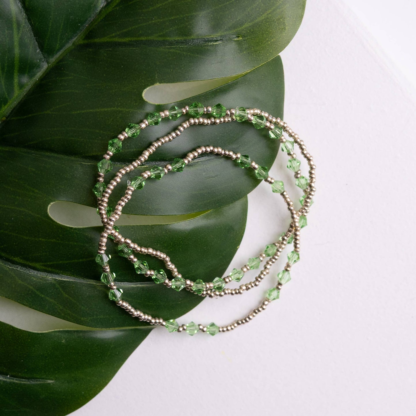 Green Cause beaded bracelet on a large green leaf with a white background
