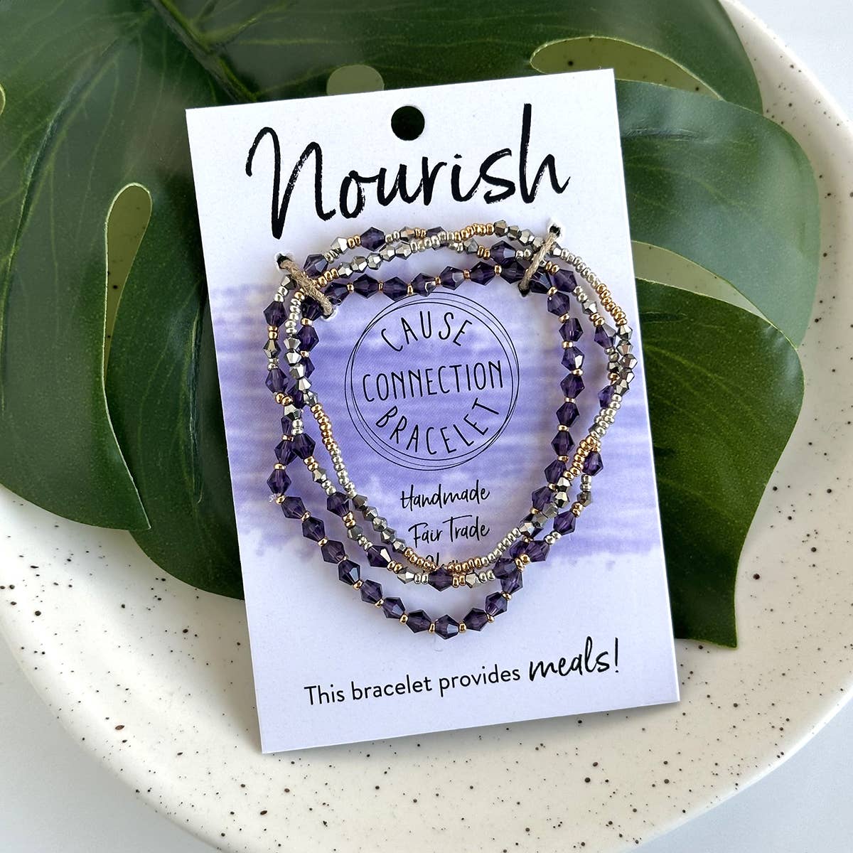 Purple handmade fair trade Nourish bracelet styled with greenery, a meaningful bracelet that provides meals and supports dignified work.