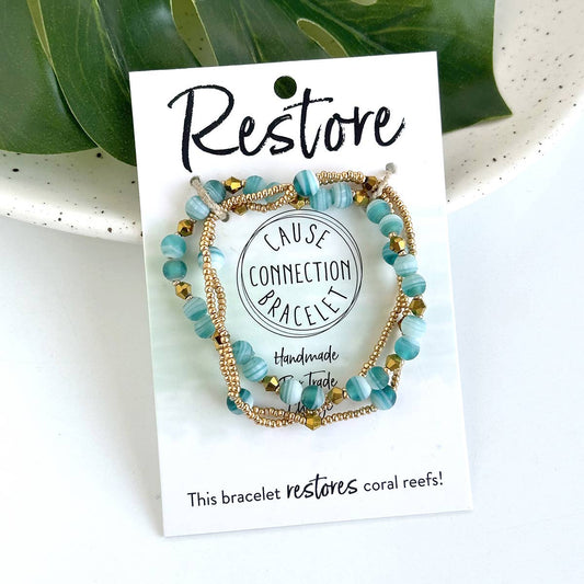Close-up of turquoise and gold handmade beaded Restore bracelet on a white card, a fair trade bracelet that helps restore coral reefs.